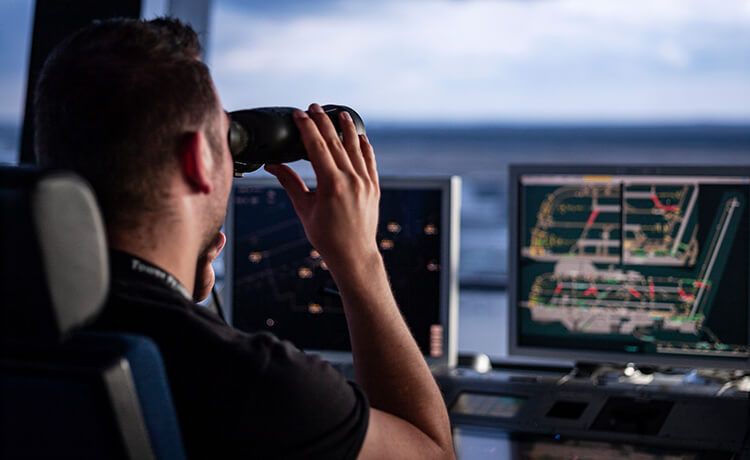 Fluglotse sitzt im Tower und beobachtet Flugzeug mit Fernglas.