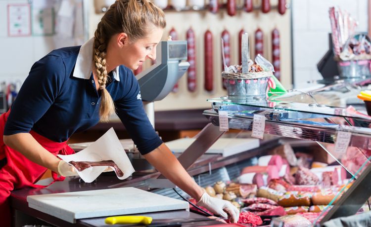 Eine Fachverkäuferin im Lebensmittelhandwerk sortiert die Fleischtheke.