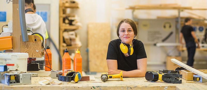 Junge Auszubildende im Handwerk lehnt auf einer Handwerk mit Werkzeug und blickt in die Kamera