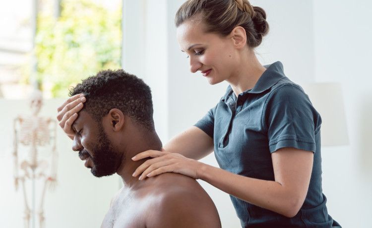Physiotherapeutin massiert den Nacken eines Patienten.